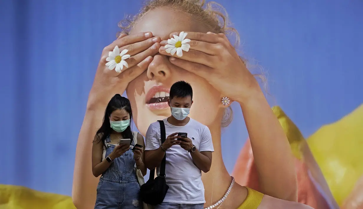 Pasangan yang memakai masker melihat ponsel mereka di depan poster besar di Hong Kong pada 27 Juli 2020. (AP Photo / Vincent Yu)