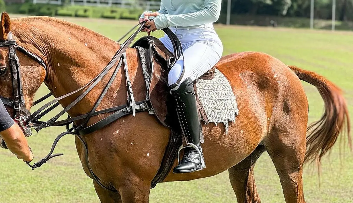 Nikita Mirzani sedang berkuda. Ia tampil anggun mengenakan baju lengkap berkuda; jaket hijau muda dan celana panjang putih. [Foto: Instagram/nikitamirzanimawardi_172]