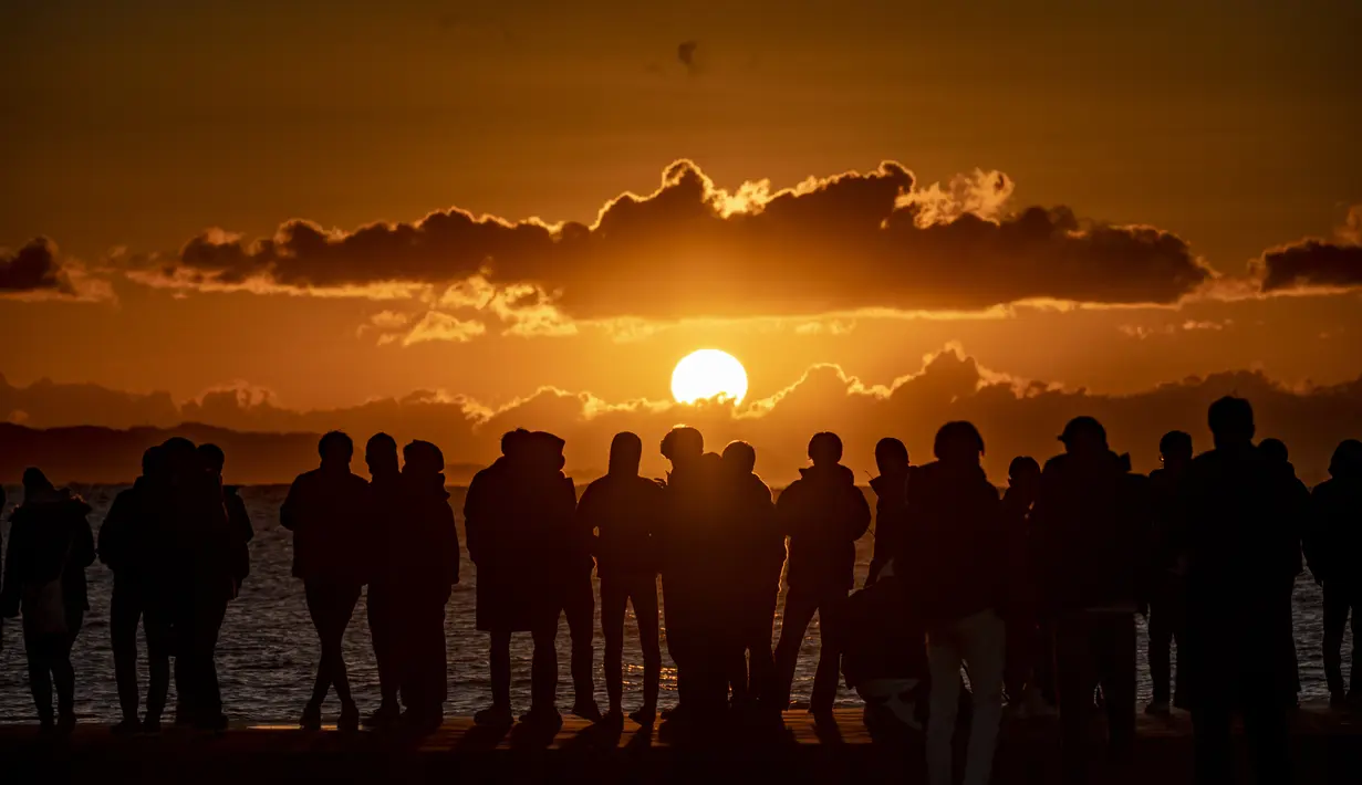 Orang-orang berkumpul di Pantai Selatan Chigasaki untuk menyaksikan matahari terbit pada Hari Tahun Baru di Prefektur Kanagawa, barat daya Tokyo (1/1/2021). Berburu matahari terbit di awal tahun tentu bisa menjadi salah satu aktivitas seru saat merayakan pergantian tahun. (AFP/Philip Fong)