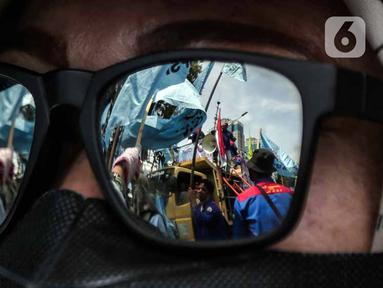 Refleksi gambar pada kacamata memperlihatkan massa buruh yang tergabung dalam Konfederasi Serikat Pekerja Seluruh Indonesia (KSPSI) dan Serikat Pekerja Nasional (SPN) demo di kawasan Patung Kuda, Jakarta, Kamis (12/5/2022). Aksi tersebut untuk memperingati May Day serta menolak Omnibuslaw UU Cipta Kerja Nomor 11 Tahun 2020 dan meminta klaster ketenagakerjaan kembali ke substansi UU Nomor 13 Tahun 2003. (Liputan6.com/Faizal Fanani)