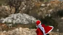 Seorang demonstran Palestina mengenakan kostum Santa Claus melempar batu ke arah pasukan keamanan Israel saat terjadi bentrokan di pos pemeriksaan Atarot di pinggiran utara Yerusalem (19/12). (AFP Photo/Abbas Momani)