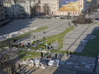 Orang-orang memasang lambang nasional Ukraina, trisula, yang terbuat dari 1,5 juta bunga tulip di alun-alun Sophiyska di pusat Kyiv, Ukraina (18/3/2022). Warga Kiev turun ke alun-alun pusat untuk menata sekitar 1,5 juta bunga tulip dalam bentuk lambang negara. (AP Photo/Efrem Lukatsky)