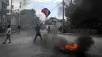 Seorang pria memegang bendera Haiti sementara ban terbakar saat demonstrasi menentang ketidakamanan di Carrefour-Feuilles, Distrik Port-au-Prince, Haiti, 14 Agustus 2023. (Richard PIERRIN/AFP)
