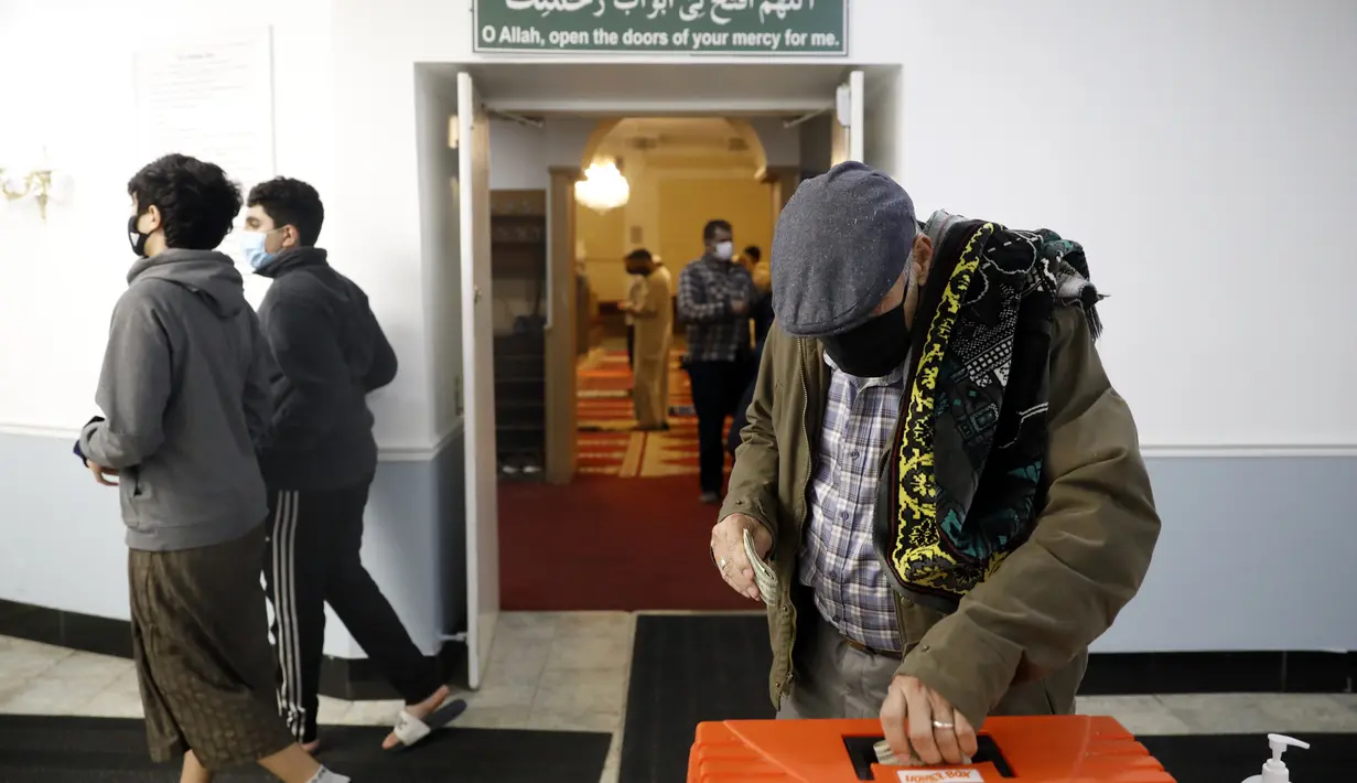 Seorang Muslim memberikan sumbangan setelah sholat tarawih ketika orang lain lewat pada malam pertama bulan suci Ramadhan di Pusat Komunitas Muslim Chicago, Senin (13/4/2021). (AP Photo/Shafkat Anowar)