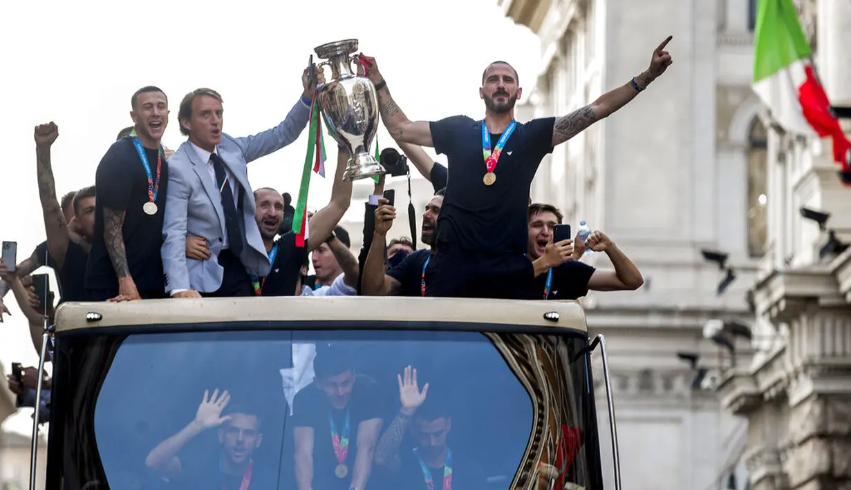 Pelatih Italia Roberto Mancini dan bek Leonardo Bonucci memegang trofi di atas bus terbuka saat perayaan juara Euro 2020 di Roma, Senin (12/7/2021). Italia mengalahkan Inggris 3-2 dalam adu penalti setelah bermain imbang 1-1 pada final Euro 2020. (Roberto Monaldo/Lapresse via AP)