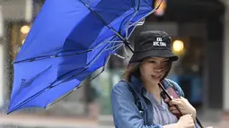 Seorang wanita membawa payungnya yang rusak saat berjalan melawan angin kencang yang ditimbulkan oleh topan Lekima di Taipei, Taiwan (9/8/2019). Topan  tersebut dinilai sebagai yang terkuat menghantam Taiwan di tahun ini. (AFP Photo/Sam Yeh)