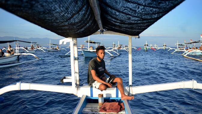 Seorang pria mengemudikan perahu saat wisata melihat lumba-lumba di perairan Pantai Lovina di Singaraja, Bali, Jumat (30/10/2020). Pantai Lovina menjadi salah satu destinasi pariwisata di Bali yang sering dikunjungi untuk menikmati matahari terbit dan lumba-lumba di laut lepas (SONNY TUMBELAKA/AFP)