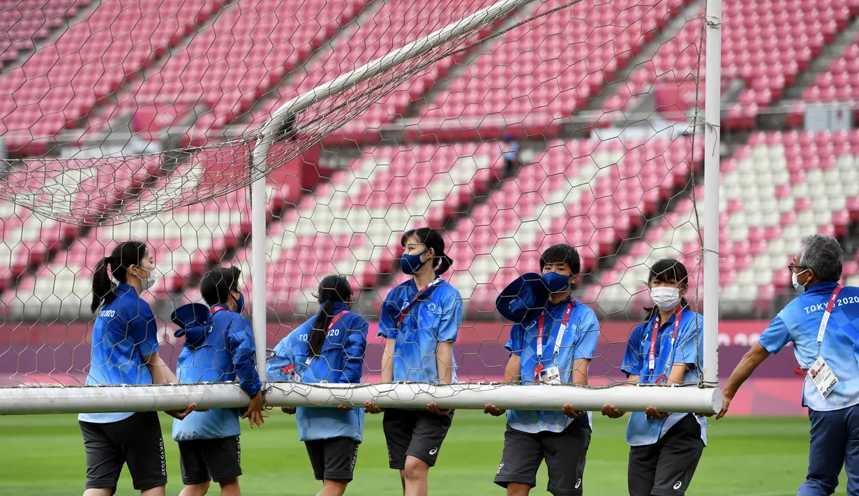 Relawan membawa tiang gawang sebelum pertandingan sepak bola putaran pertama grup G putri Olimpiade Tokyo 2020 antara AS dan Australia di Stadion Ibaraki Kashima di kota Kashima, pada 27 Juli 2021. Relawan atau volunteer merupakan salah satu kunci suksesnya suatu perhelatan. (SHINJI AKAGI/AFP)