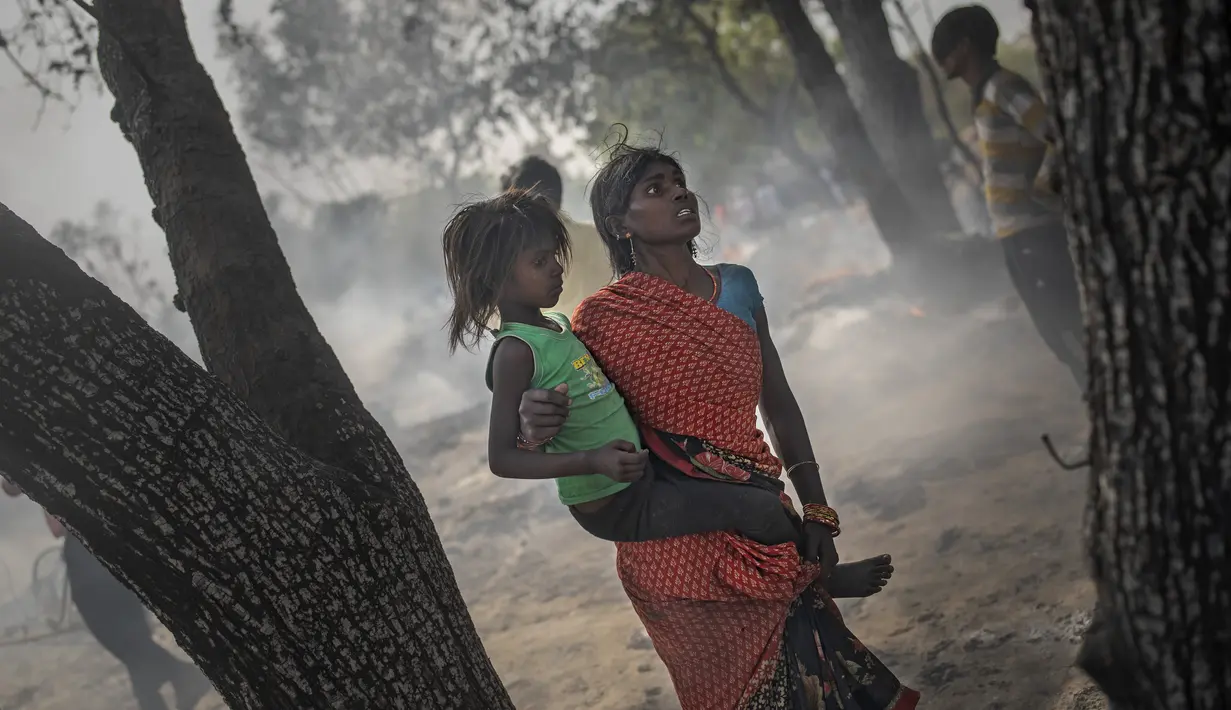 Seorang wanita menggendong putrinya saat terjadi kebakaran di daerah kumuh di Noida, pinggiran New Delhi, India, Minggu (11/4/2021). Dua anak tewas dan lebih dari 150 gubuk kumuh yang sebagian besar dihuni oleh para pemulung dalam kebakaran pada Minggu sore. (AP Photo/Altaf Qadri)