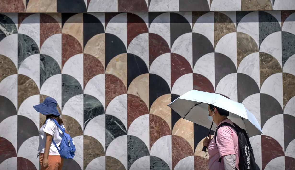 Orang-orang menggunakan topi matahari dan payung untuk melindungi diri dari sinar matahari saat mereka berjalan di luar pusat perbelanjaan pada hari yang panas di luar musimnya di Beijing, Sabtu, 24 Juni 2023. (AP Photo/Mark Schiefelbein)