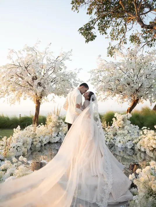 Sentuhan couture semakin terasa lewat detail panel pleated pada bagian samping rok yang menyerupai kelopak bunga raksasa. Elemen ini memberikan dimensi unik yang membuat gaun Jennifer tampil berbeda dari wedding gown klasik pada umumnya. [@jennifercoppenreal20].