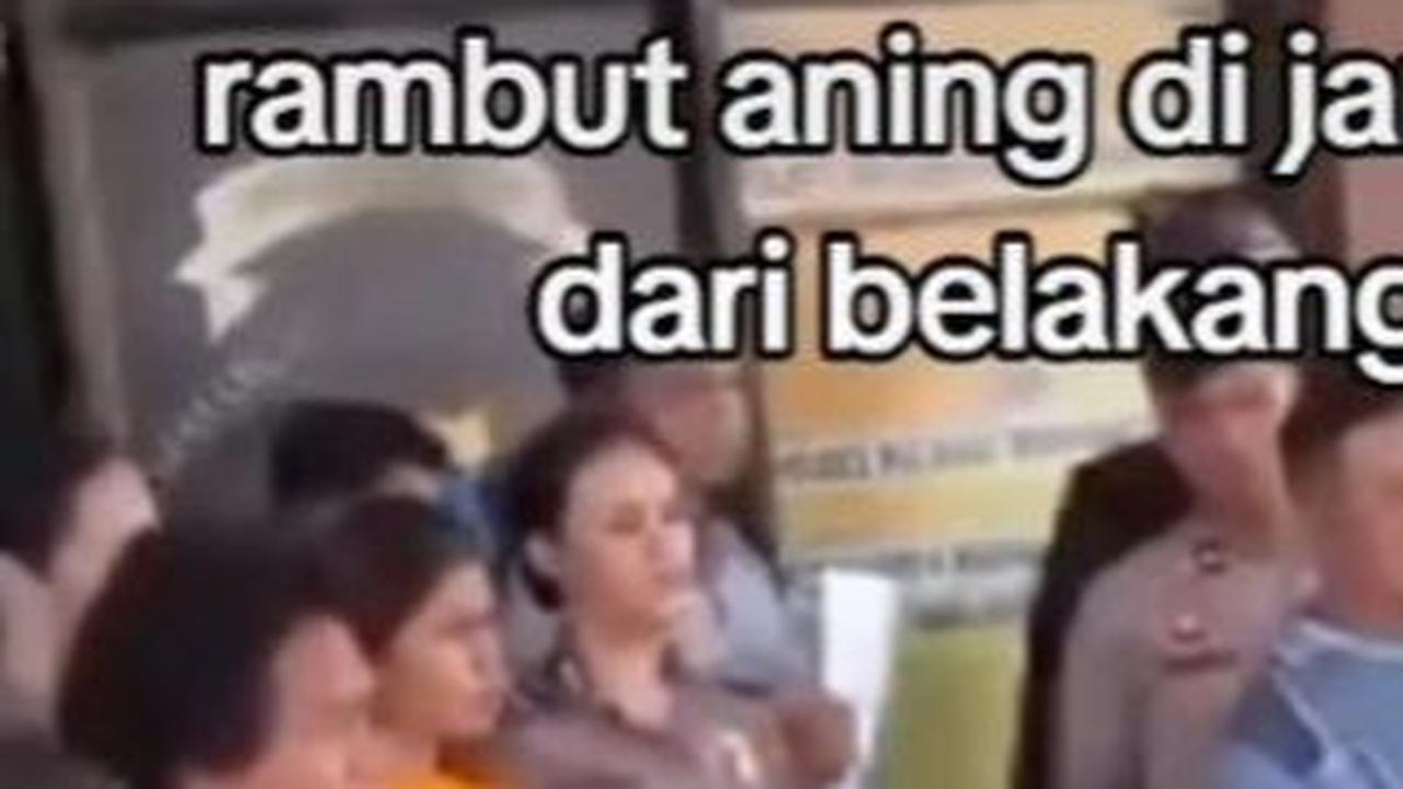 Mengenakan baju orange, Aning terlihat didampingi oleh polisi saat berdiri di depan kantor polisi.