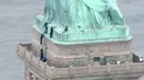 Petugas kepolisian membujuk seorang wanita yang memanjat Patung Liberty di New York, Rabu (4/7). Aksi wanita bernama Therese Okoumou ini memprotes kebijakan imigrasi pemerintah Presiden Donald Trump yang memisahkan keluarga migran. (AFP/PIX11 News/HO)