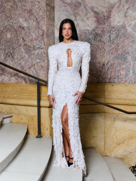 Dua memadukan penampilannya dengan anting statement dan sepatu hak tinggi hitam. Tata riasnya menghadirkan bold brows, riasan mata minimalis, dan bibir mengilap, sementara rambutnya dibiarkan terurai alami dengan belahan tengah yang effortless.  [@dualipa].