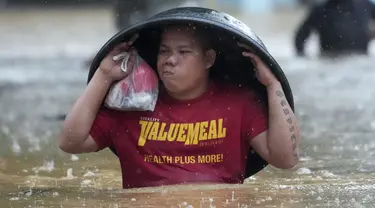 Seorang warga menggunakan bak cucian untuk melindunginya dari hujan saat ia menyeberangi jalan yang banjir akibat Badai Tropis Yagi, yang secara lokal disebut Enteng, di Cainta, provinsi Rizal, Filipina, Senin (2/9/2024). (AP Photo/Aaron Favila)