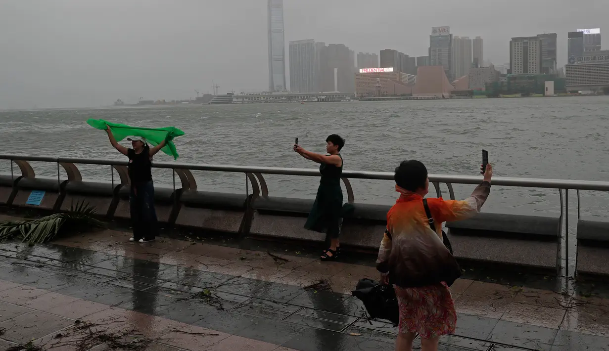Warga berselfie setelah angin kencang yang disebabkan oleh angin topan Hato menerjang tepi pantai Victoria Habour di Hong Kong, (23/8). Embusan angin akibat topan Hato mencapai kecepatan 86 kilometer hingga 103 kilometer per jam. (AP Photo/Vincent Yu)