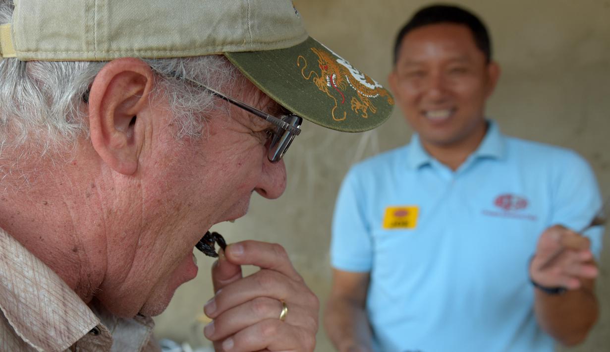 Seorang turis memakan tarantula goreng di wilayah Skun, Provinsi Kampong Cham, Kamboja, 14 Maret 2018. Warga Kamboja terbiasa mengonsumsi tarantula goreng sebagai camilan. (TANG CHHIN Sothy / AFP)