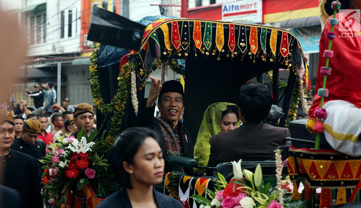 Presiden Joko Widodo bersama Ibu Negara Iriana saat membagikan kaus di atas kereta kencana saat kirab resepsi pernikahan Kahiyang Ayu-Bobby Nasution di Kota Medan, Sumatera Utara, Minggu (26/11). (Liputan6.com/Johan Tallo)