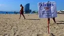 Seorang pria melewati sebuah spanduk menyerukan gerakan anti-wisatawan di pantai Barcelona, Sabtu (12/8). Para aktivis menggelar aksi protes di tempat-tempat populer Spanyol melawan ledakan industri pariwisata yang tak terkendali (AP Photo/Manu Fernandez)