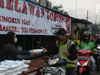 Warga menerima pembagian nasi bungkus gratis di Posko Perjuangan Rakyat (POSPERA), Jakarta, Rabu (10/3/2021). Pembagian 500 nasi bungkus beserta masker dan vitamin secara gratis setiap harinya dalam bentuk meringankan beban warga di tengah pandemi Covid-19. (merdeka.com/Imam Buhori)