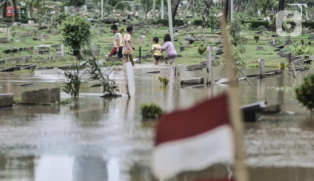 Anak-anak bermain saat banjir merendam TPU Karet Bivak, Jakarta, Minggu (7/2/2021). Banjir yang terjadi di TPU Karet Bivak untuk kedua kalinya tersebut juga menyulitkan mereka yang ingin melakukan ziarah ke makam keluarga maupun kerabat. (merdeka.com/Iqbal Nugroho)