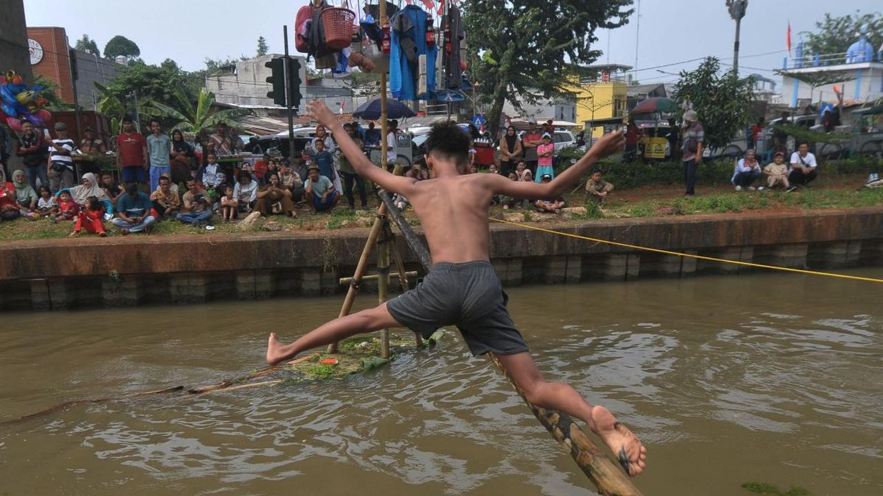 Seorang peserta mencoba melewati bambu yang telah dilumuri oli untuk mencapai pinang dalam lomba Titian Bambu di aliran Kalimalang, Jakarta Timur, Sabtu (24/8/2024). Semangat perayaan HUT ke-79 Kemerdekaan RI masih terasa di lingkungan RW 04 Kelurahan Cip