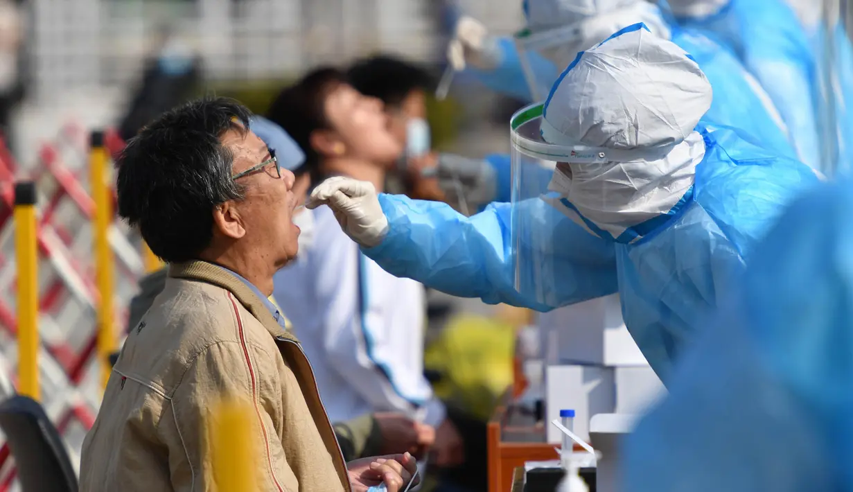 Petugas medis mengambil sampel warga saat tes COVID-19 di Qingdao, China, Senin (12/10/2020). Lebih dari 9 juta orang yang tinggal di kota Qingdao menjalani tes COVID-19 secara massal setelah kasus baru muncul terkait dengan rumah sakit yang merawat pasien terinfeksi dari luar negeri. (STR/AFP)