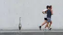 Dua pelari berlari melewati bangau kelabu di depan sebuah gedung di distrik pemerintah di Berlin, Jerman pada 30 Juli 2020. (Fabian Sommer / dpa via AP)