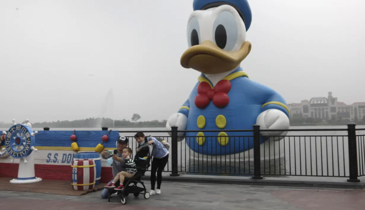 Wisatawan berswafoto di depan patung Donald Duck di taman hiburan Disneyland, Shanghai, China, Senin (11/5/2020). Saat ini Disneyland Shanghai hanya menerima pengunjung kurang dari 24 ribu orang, atau 30 persen dari kapasitas harian. (AP Photo/Chen Si)