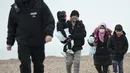 Para migran berjalan di sepanjang pantai setelah dibantu ke darat dari sekoci RNLI (Royal National Lifeboat Institution) menyusul penyelamatan mereka saat melintasi Selat Inggris di Dungeness, Inggris tenggara (24/11/2021). (AFP/Ben Stansall)