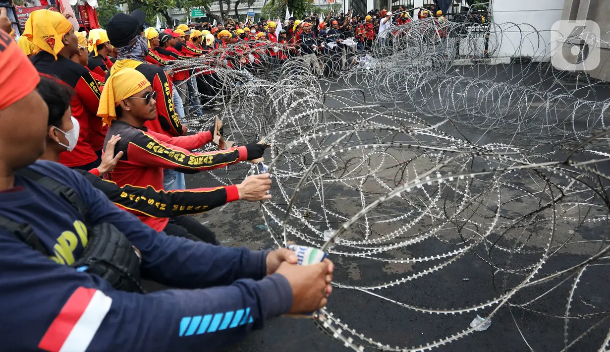Massa merusak pagar berduri saat berunjuk rasa di depan Gedung DPR, Senayan, Jakarta, Selasa (14/3/2023). Imbas aksi demo tersebut, kepolisian mengimbau kepada para pengguna jalan untuk mencari jalan alternatif guna menghindari kemacetan. (Liputan6.com/Johan Tallo)