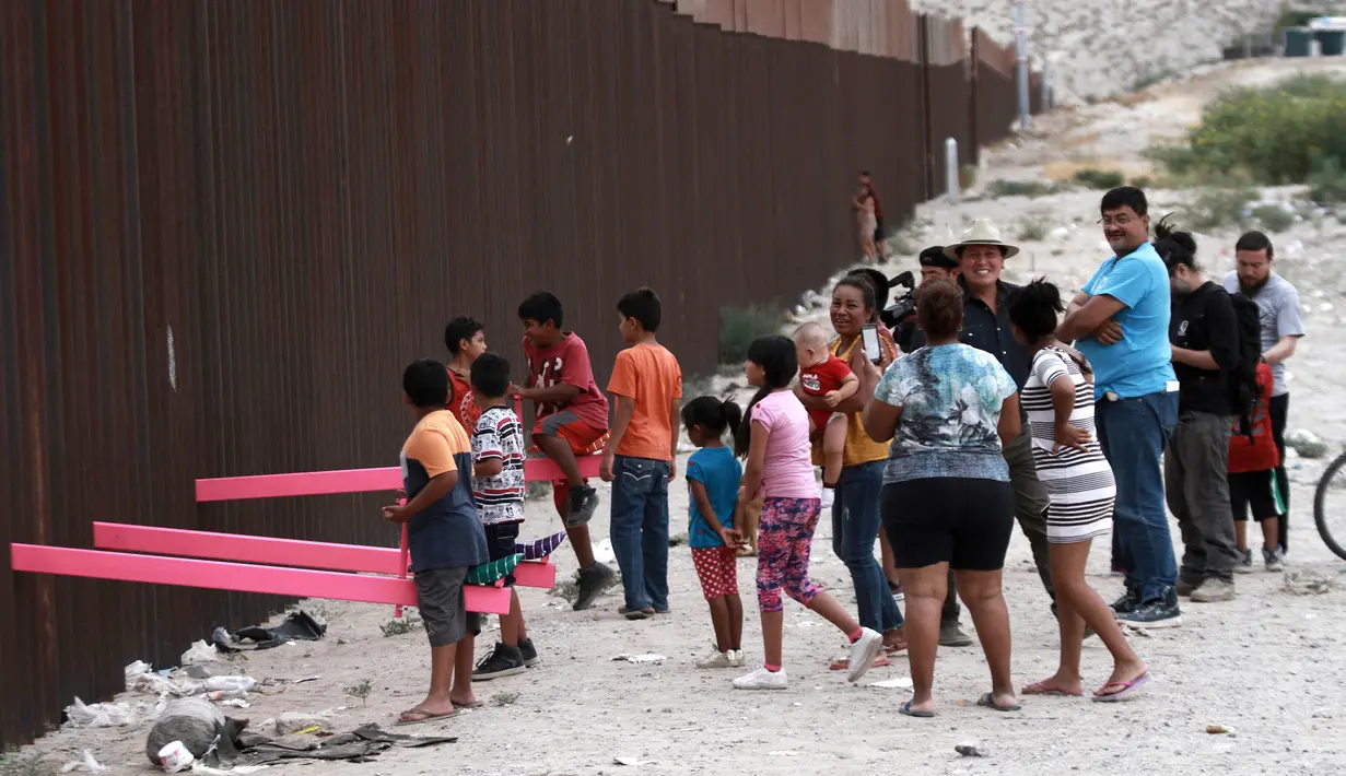 Suasana saat anak-anak bermain jungkat-jungkit yang dipasang di antara pagar pemisah Meksiko dengan Amerika Serikat, Ciudad de Juarez, Meksiko, Minggu (28/7/2019). Jungkat-jungkit tersebut dirancang seorang profesor arsitektur California, Ronald Rael. (AP Photo/Christian Chavez)