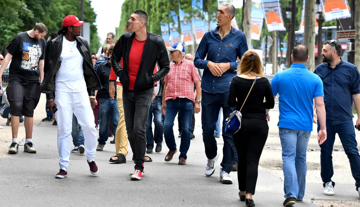 Sejumlah pria tertinggi di dunia berjalan di tengah keramaian di Champs-Elysees Avenue, Paris, 1 Juni 2018. Belasan pria tertinggi di dunia bertemu pada akhir pekan di ibu kota Prancis. (AFP/GERARD JULIEN)