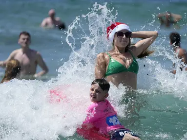 Pengunjung asal Inggris Sophie Woodward (kanan) mengenakan topi Santa saat bermain di air bersama sepupunya Maxi Woodward di Pantai Bondi di Sydney, Senin, 25 Desember 2023. (AP Photo/Rick Rycroft)