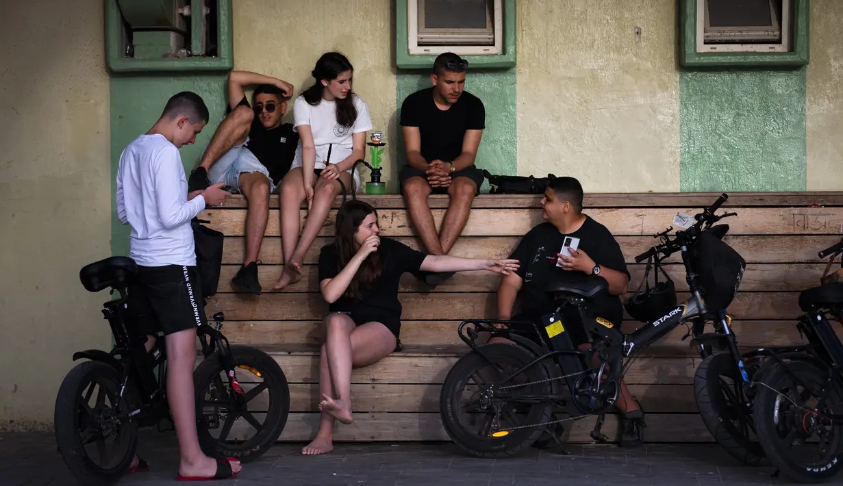 Pemuda Israel tanpa masker menikmati hari yang cerah di pantai Tel Aviv, Minggu (18/4/2021). Israel mencabut aturan wajib masker di ruang publik dan membuka kembali sekolah sepenuhnya dalam upaya menuju normalisasi setelah kampanye vaksinasi Covid-19 berjalan sukses. (AP Photo/Oded Balilty)