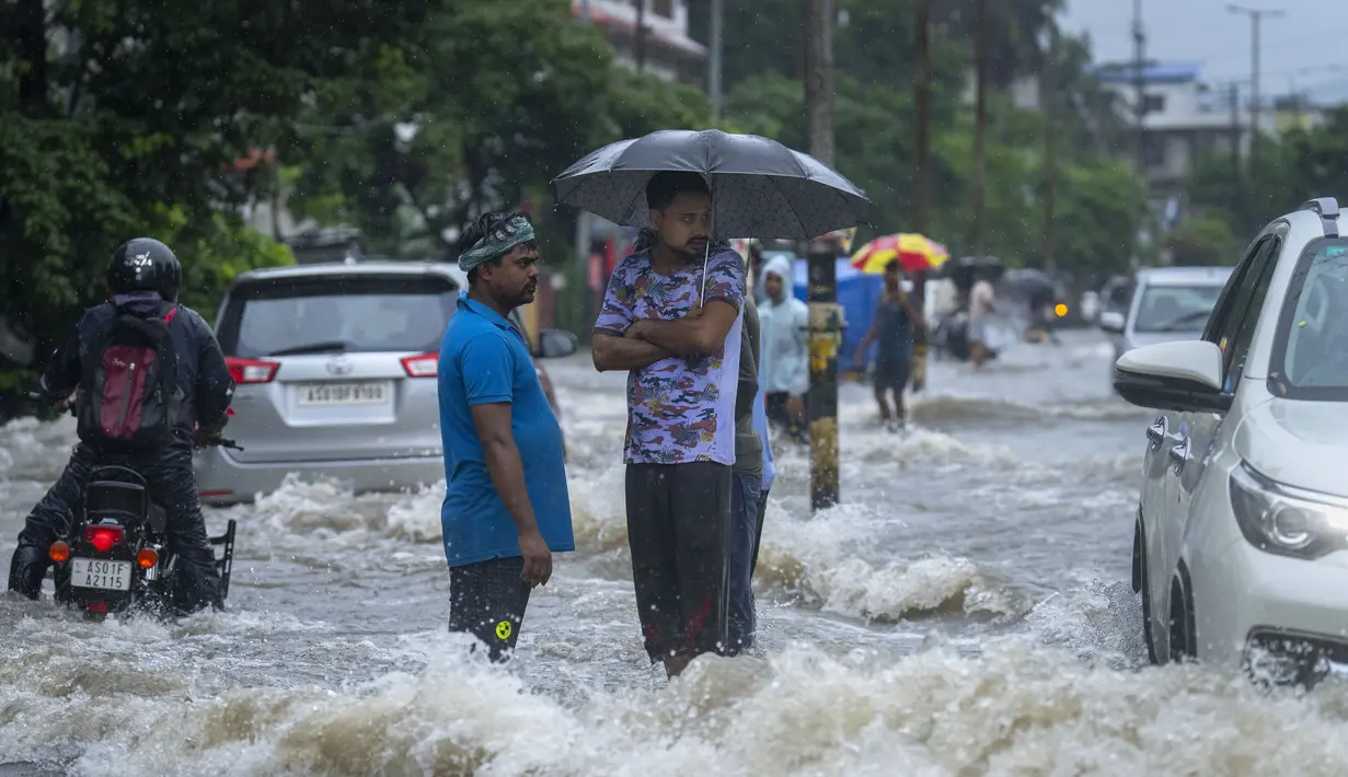 Warga berdiri di jalan yang tergenang air saat hujan deras di Guwahati, negara bagian Assam, India, Kamis (16/6/2022). Guwahati telah menerima curah hujan 81,5 mm dalam 24 jam terakhir yang termasuk dalam kategori 'hujan lebat' dalam 24 jam terakhir. (AP Photo/Anupam Nath)