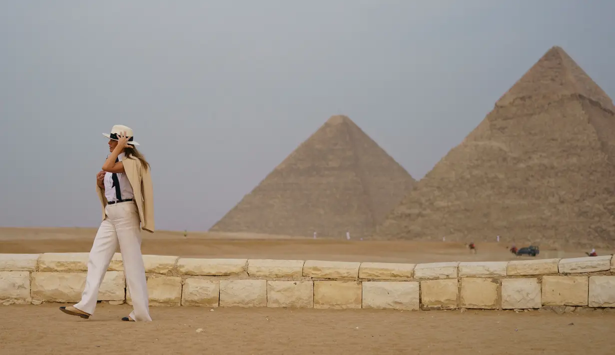 Ibu Negara AS Melania Trump memegang topinya saat berkunjung ke situs bersejarah Piramida Giza, Kairo, Mesir (6/10). Melania tampil mengenakan busana safari klasik saat mengunjungi destinasi terakhir selama seminggu di Afrika. (AP Photo/Carolyn Kaster)