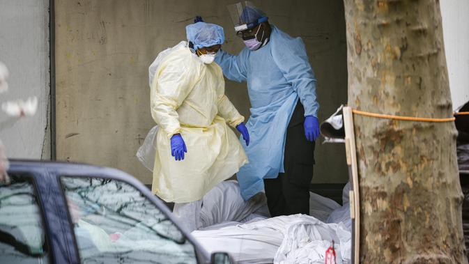 Petugas melangkahi sejumlah jenazah yang diduga korban virus corona COVID-19 dalam trailer berpendingin di Kingsbrook Jewish Medical Center, Brooklyn, New York, AS, 3 April 2020. Menurut Universitas Johns Hopkins, total kasus COVID-19 secara global sebanyak 1.286.409. (AP Photo/John Minchillo)