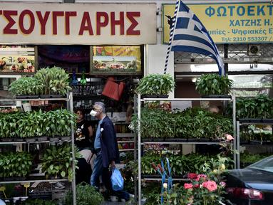 Seorang pejalan kaki berjalan di jalan mengenakan masker di pusat Thessaloniki, Yunani utara (18/5/2022). Sebuah komite ahli dari Kementerian Kesehatan sedang memeriksa kemungkinan melonggarkan mandat masker pada 1 Juni, menyusul penurunan Covid19. (AFP/Sakis Mitrolidis)