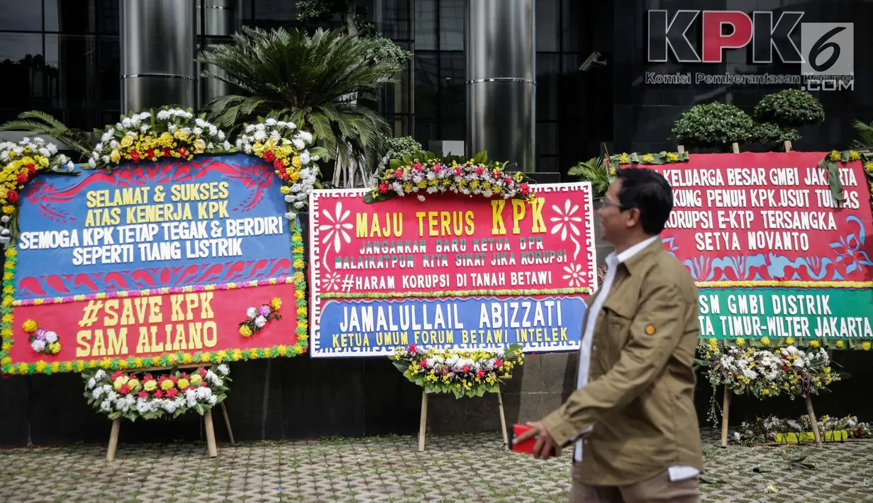 Warga melintas dekat karangan bunga berisi dukungan pada KPK di halaman Gedung KPK, Jakarta, Senin (20/11). Karangan bunga tersebut sebagai bentuk dukungan masyarakat kepada KPK terhadap pemberantasan kasus korupsi e-KTP. (Liputan6.com/Faizal Fanani)