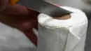 Seorang karyawan memotong kue berbentuk tisu toilet di toko roti Schuerener Backparadies di Dortmund, Jerman, 26 Maret 2020. Kelangkaan kertas tisu toilet memunculkan ide bagi pemilik toko roti itu, Tim Kortuem, membuat kue menyerupai barang yang diburu warga di tengah Covid-19. (Ina FASSBENDER/AFP