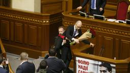 PM Arseny Yatsenyuk tampak digendong dan disingkirkan paksa oleh seorang anggota parlemen, Oleg Barna dari atas podium Majelis Tinggi Parlemen Ukraina, 11 Desember 2015. PM Yatseniuk yang kaget terlihat berpegangan pada podium. (REUTERS/Valentyn Ogirenko)