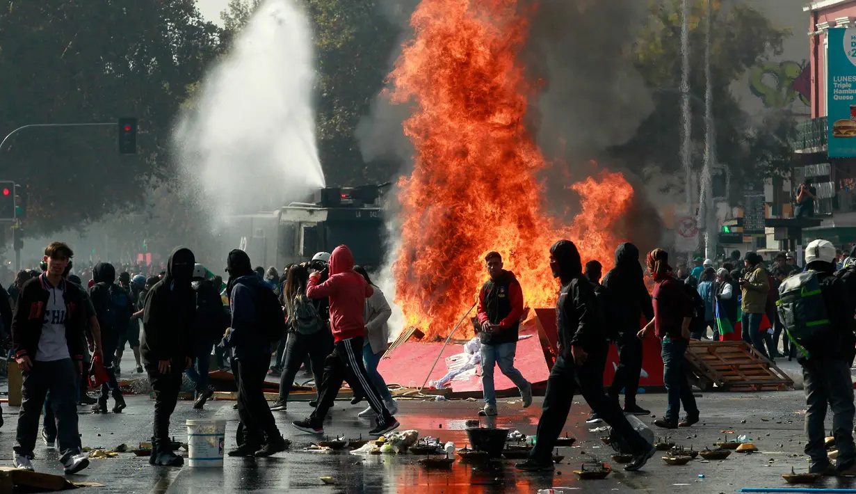 Api menyala di dekat demonstran setelah terjadi bentrokan saat peringatan Hari Buruh di Santiago, Chili (1/5). Hari buruh tahunan ini berawal dari usaha gerakan serikat buruh untuk merayakan keberhasilan ekonomi dan sosial para buruh. (AFP/Claudio Reyes)
