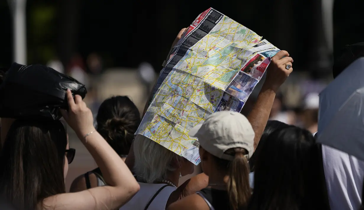 <p>Seorang turis menggunakan peta pusat kota London untuk menutupi kepalanya dari matahari sambil menunggu menyaksikan upacara Pergantian Penjaga di luar Istana Buckingham, selama cuaca panas di London, Senin (18/7/2022). Pemerintah Inggris telah mengeluarkan peringatan "merah" pertama mereka untuk panas ekstrem. (AP Photo/Matt Dunham)</p>