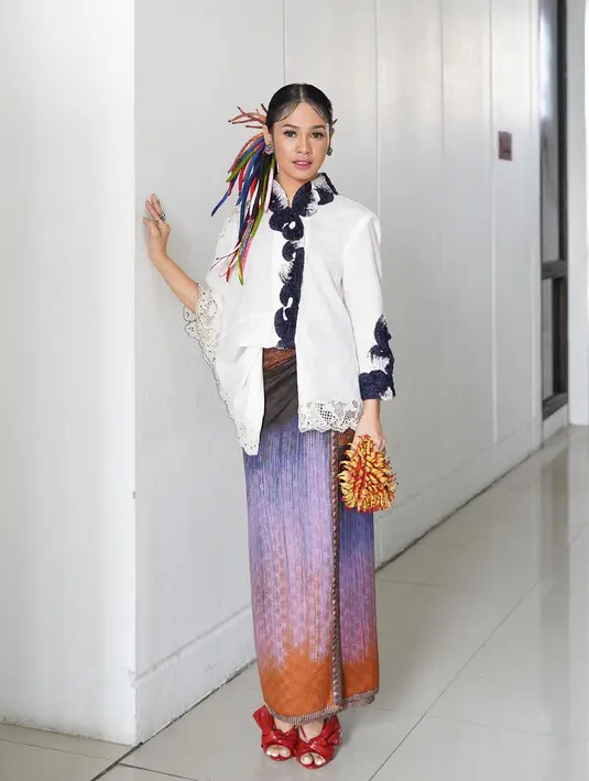 Padu padan menarik dari Andien saat mengenakan kebaya encim. Kebaya encim pilihan Andien juga memiliki siluet modern, berwarna putih dengan aksen di bagian leher dan lengan. Andien memadukan penampilannya ini dengan kain batik bernuansa gradasi yang tak kalah cantik, heels merah, dan tas tangan yang unik. [Foto: Instagram/andienaisyah]