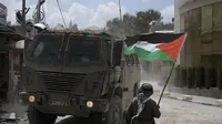 Seorang pria melambaikan bendera Palestina saat kendaraan lapis baja Israel bergerak selama operasi militer di kamp pengungsi Nur Shams, Tulkarem, Tepi Barat yang diduduki pada Kamis (29/8/2024). (Dok. AP/Majdi Mohammed)