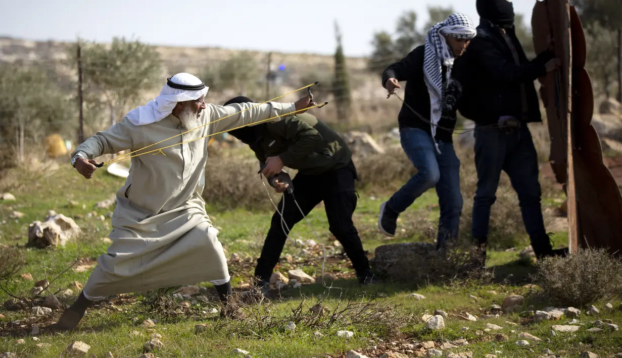 Pengunjuk rasa Palestina menggunakan ketapel untuk melemparkan batu ke arah pasukan Israel selama protes terhadap permukiman Israel, di desa Deir Jarir Tepi Barat, utara Ramallah, Jumat (1/1/2021). Setidaknya 16 warga Palestina terluka akibat bentrokan tersebut. (AP Photo/Majdi Mohammed)