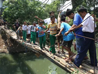 Sejumlah pelajar menyeberangi Kali Angke melewati jembatan rapuh di Kampung Cantiga, Petir, Cipondoh, Tangerang, Rabu (2/9/2015). Jembatan berusia lima tahun tersebut menghubungkan Cipondoh dan Kembangan, Jakarta. (Liputan6.com/Gempur M Surya)