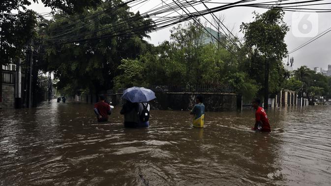 Warga melintasi banjir di Jalan Hang Lekir, Kebayoran Lama, Jakarta Selatan, Rabu (1/1/2020). Banjir tersebut disebabkan karena tingginya intensitas hujan yang mengguyur sejak Selasa (31/12/2019). (Liputan6.com/Johan Tallo)