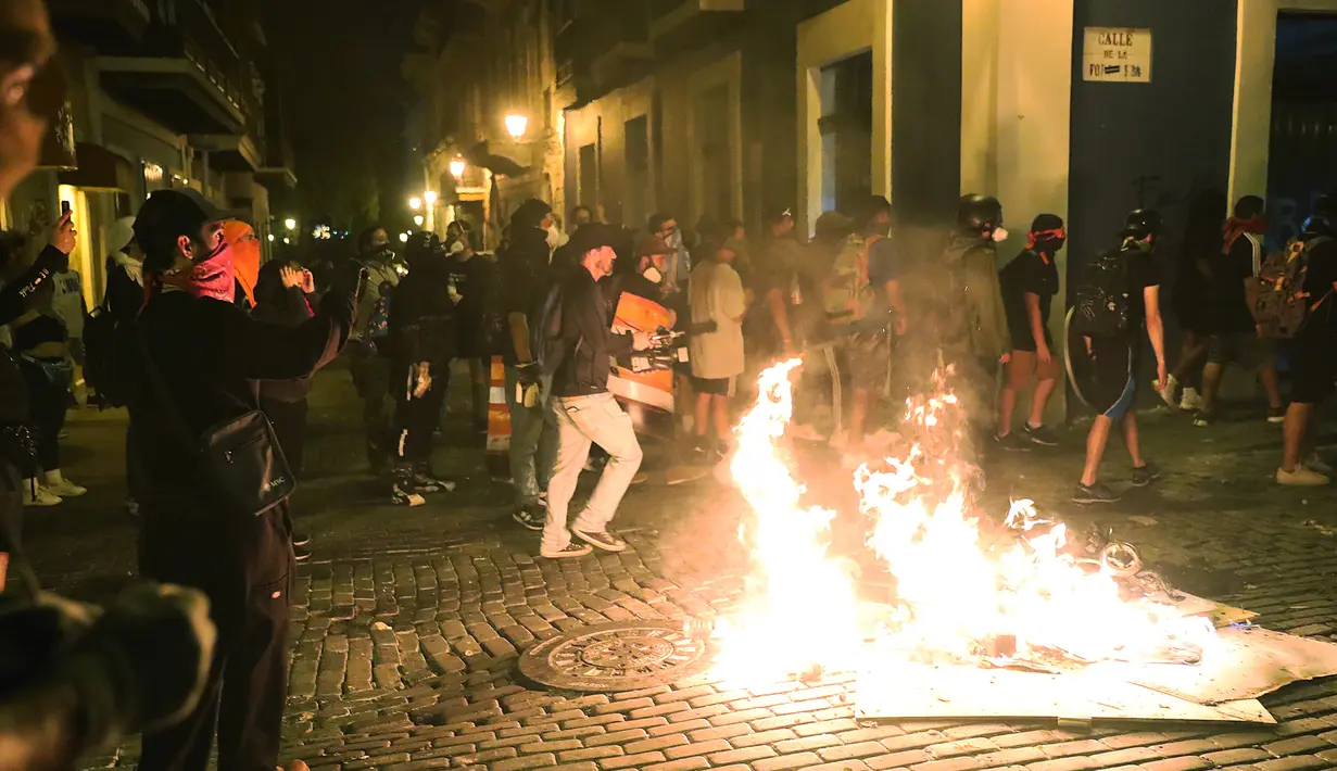Para pengunjuk rasa membakar sampah saat bentrok dengan polisi di Old San Juan, Puerto Rico (22/7/2019). Para pengunjuk rasa menuntut agar Gubernur Ricardo Rossello mundur  dari jabatannya setelah dalam pusaran skandal pesan teks daring tak senonoh dengan para stafnya. (AFP Photo/Joe Raedle)